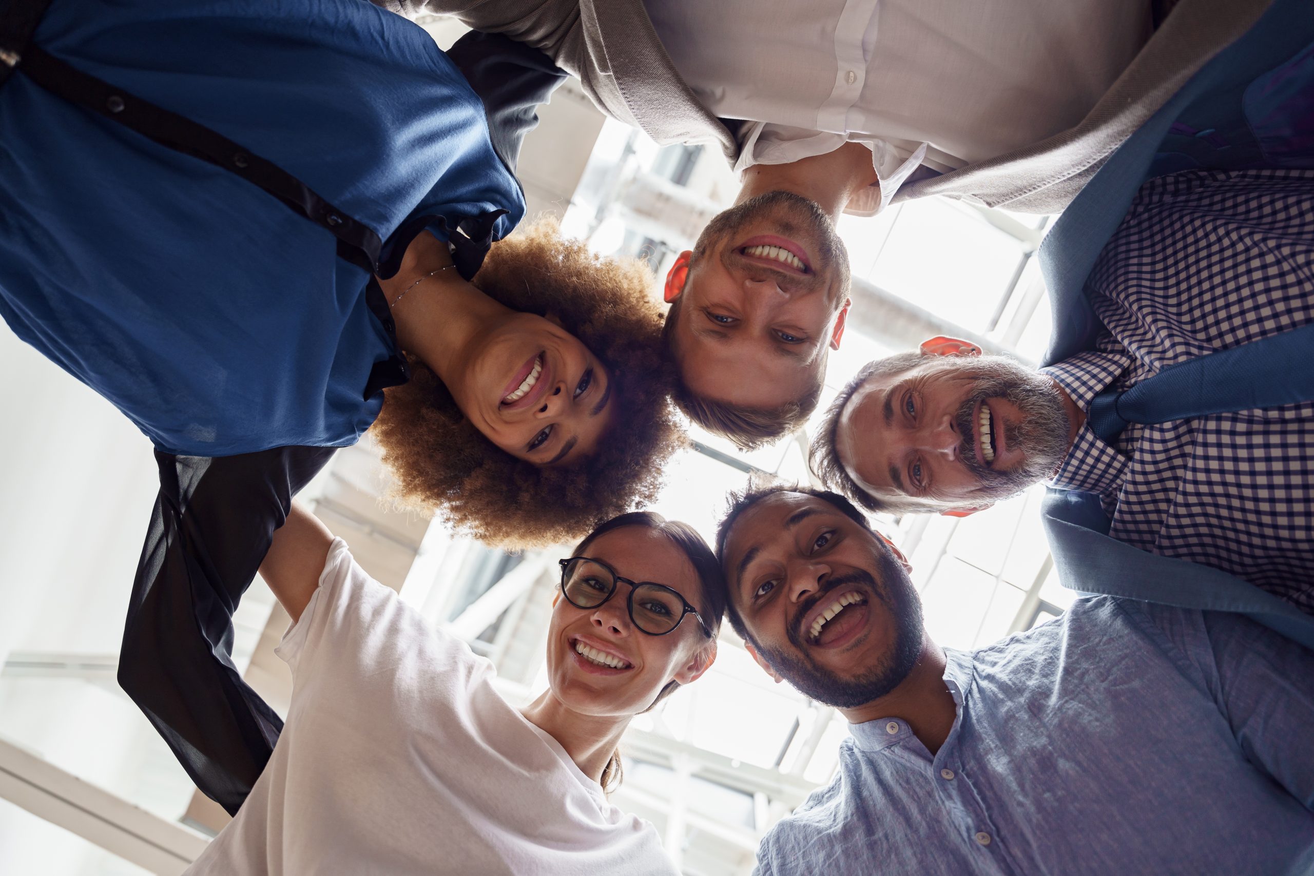 Below view of several happy business partners looking at camera while embracing each other